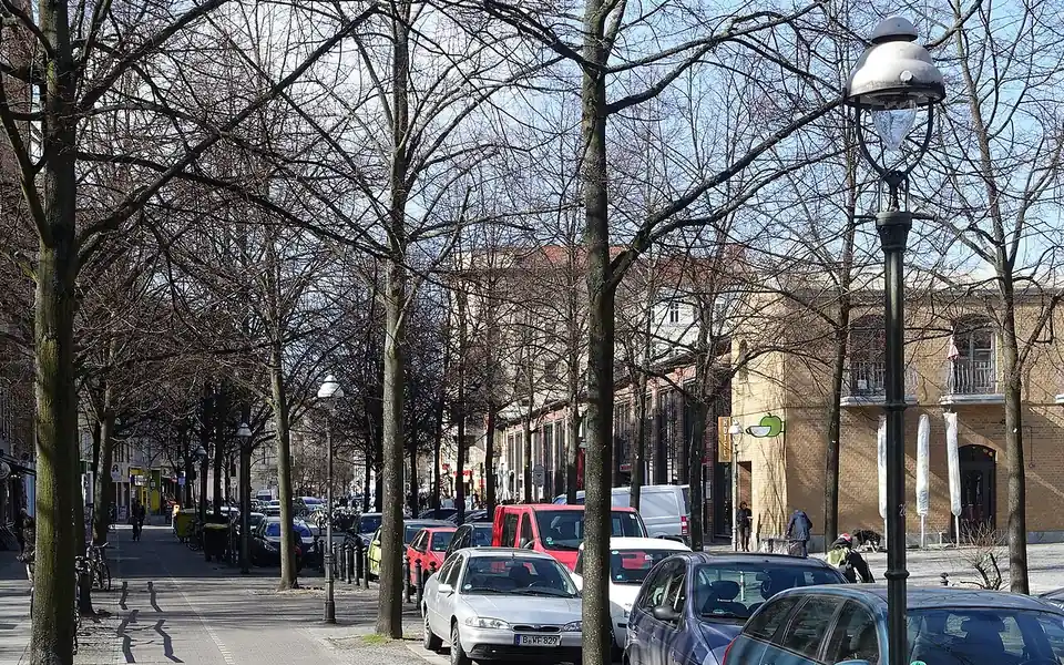A tree-lined pavement, street lamps and parked cars on Bergmannstraße in Berlin