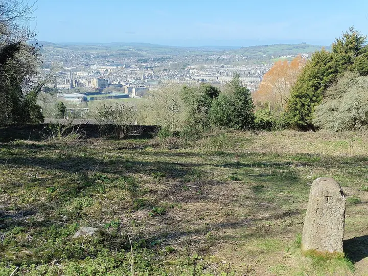 Bath buildings in a valley, viewed across a grassy hillside.
