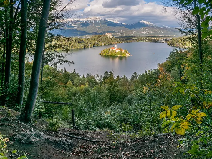 Church on an island in Lake Bled, framed by trees and distant hills.