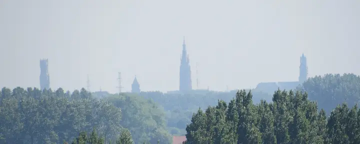 Distant church towers of Bruges above trees in the haze.