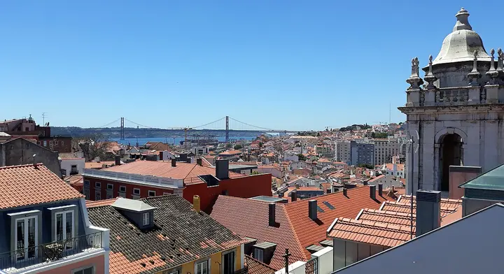 Red rooftops of Lisbon with a suspension bridge in the distance.