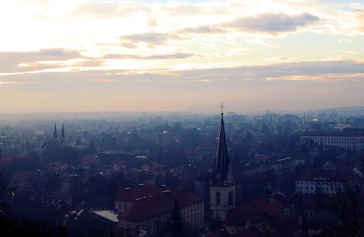 Ljubljana rooftops and a church spire beneath the evening sky.