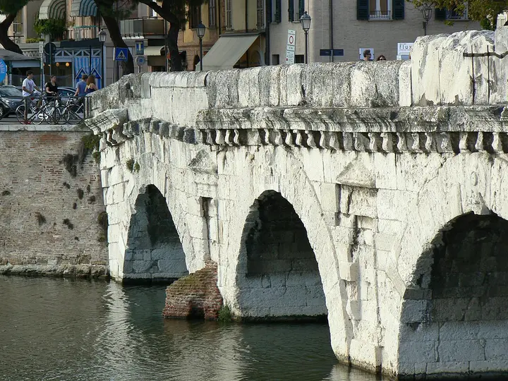 Stone arches of the Tiberius Bridge spanning water in Rimini.