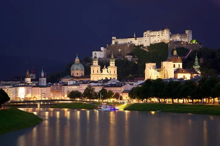Illuminated fortress and Salzburg buildings across the river at night.