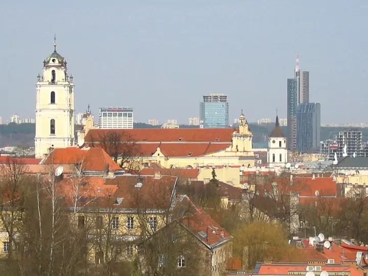 Church towers and red rooftops in Vilnius with modern buildings beyond.